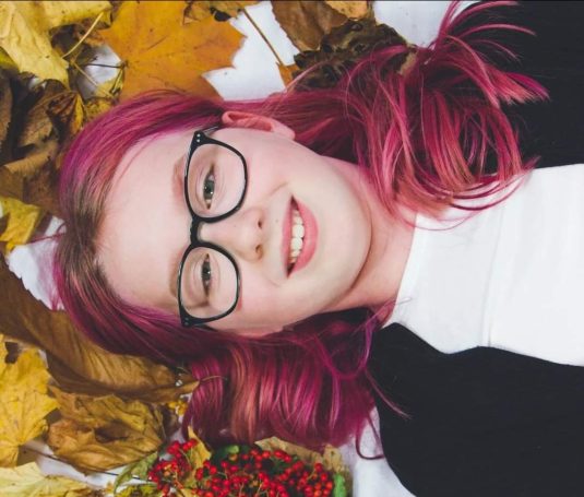 Young girl with purple hair and glasses lay in autumn leaves