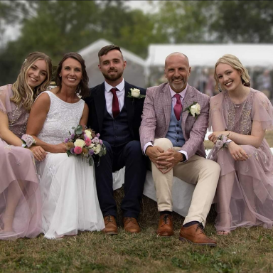 Wedding couple with best man and bridemaids sat on bales of hay