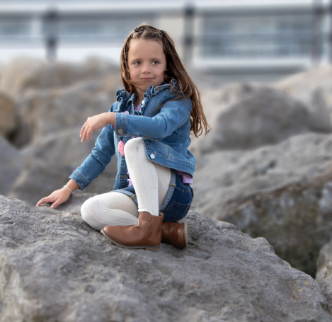 Young girl denim shorts and jacket sat on rocks