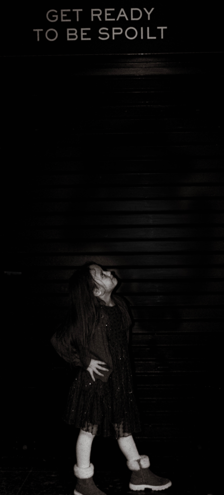 young girl looking up at sign saying get ready to be spoilt. Picture is black and white.