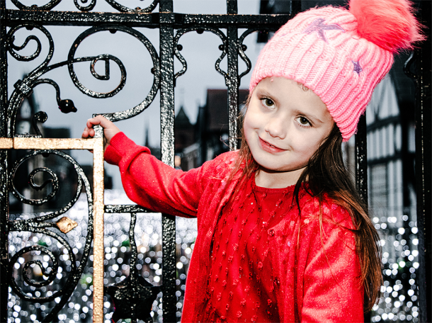 Young girl in red clothing with winter hat standing next to ornate iron fencing